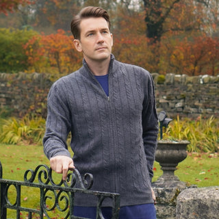 Man wearing a gray cashmere zip sweater standing in a garden of an English country house